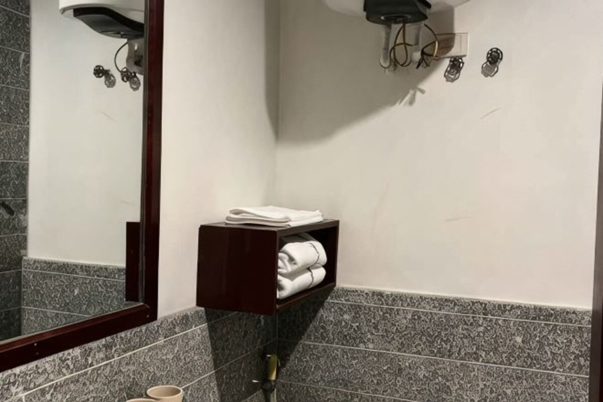 Une salle de bain avec un mur recouvert de carreaux de marbre, une étagère en bois foncé où sont pliées des serviettes, et un miroir qui reflète la pièce.