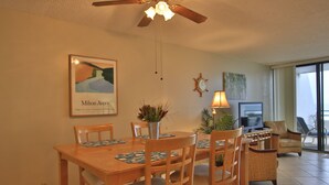 Zona pranzo con tavolo e sedie in legno, una ventola a soffitto, una televisione e una finestra con vista.