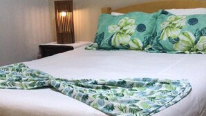 A neatly made bed with a floral bedspread and pillows, a bedside table with a lamp, and a wall painting. - Rancho - Mini stud farm with swimming pool and barbecue! (Sao pedro)