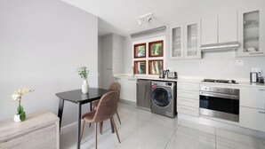 Cozinha moderna com armários brancos, forno embutido, máquina de lavar roupa e área de refeições com mesa e cadeiras.