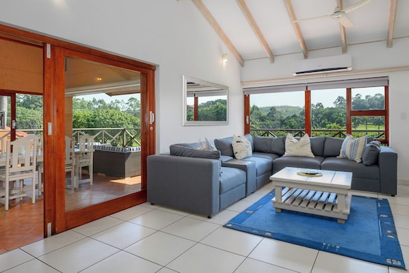 A spacious living area with a sofa set, a dining table, and a view of the outdoors.