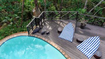Une terrasse en bois avec une piscine, entourée d’une végétation luxuriante.