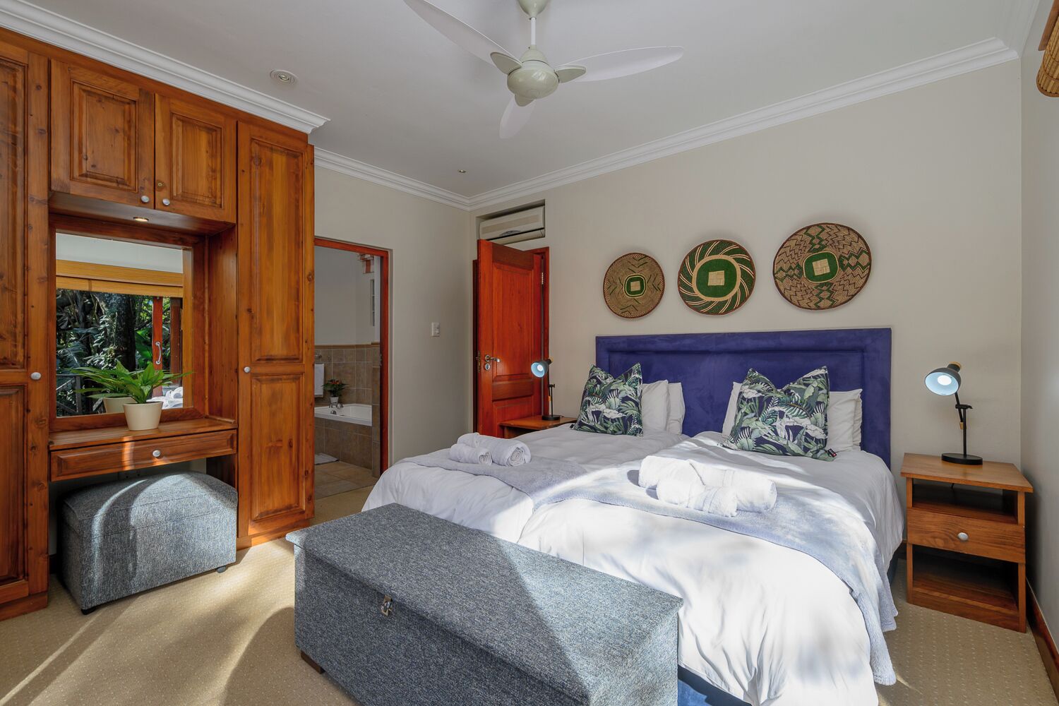 A bedroom with a bed, bedside tables, a dresser, a mirror, and decorative wall art.