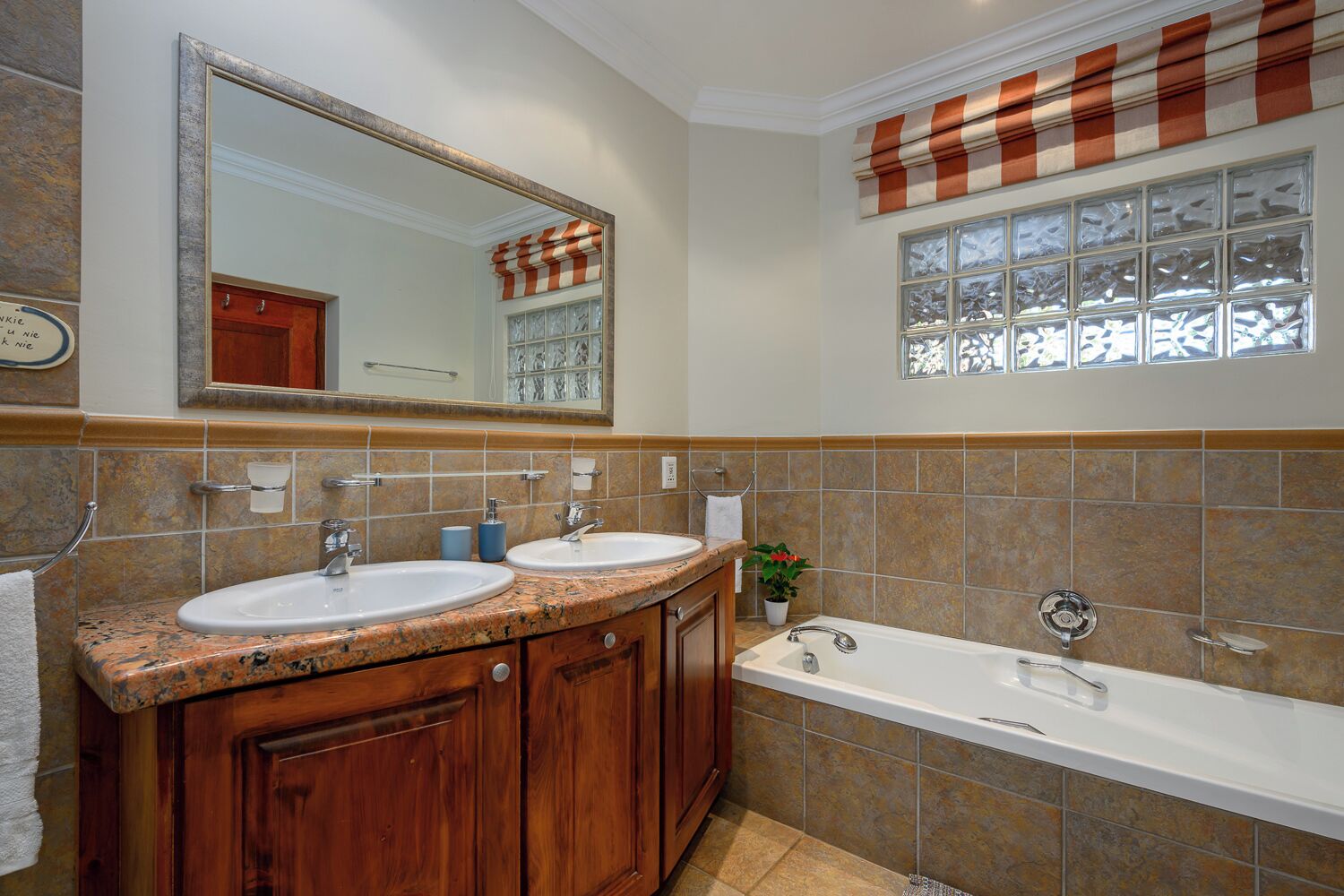 A bathroom with two sinks, a large mirror, a window with blinds, and a bathtub.