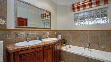 A bathroom with two sinks, a large mirror, a window with blinds, and a bathtub.