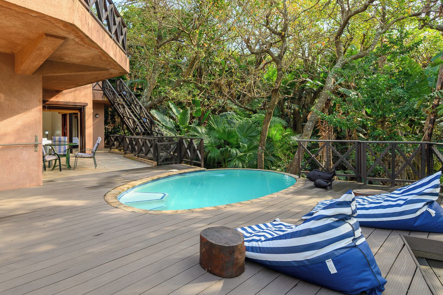 A wooden deck with a swimming pool, lounge chairs, and a staircase leading to a building.