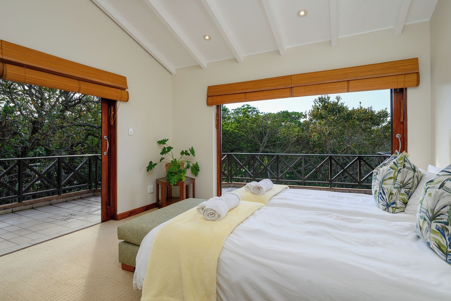 Une chambre avec un grand lit, une petite table sur laquelle est posée une plante, et un balcon doté d’une balustrade.