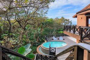 A pool area with a wooden deck, lounge chairs, and a view of the surrounding forest. - San Lameer Villa Rentals 11703 (Southbroom)