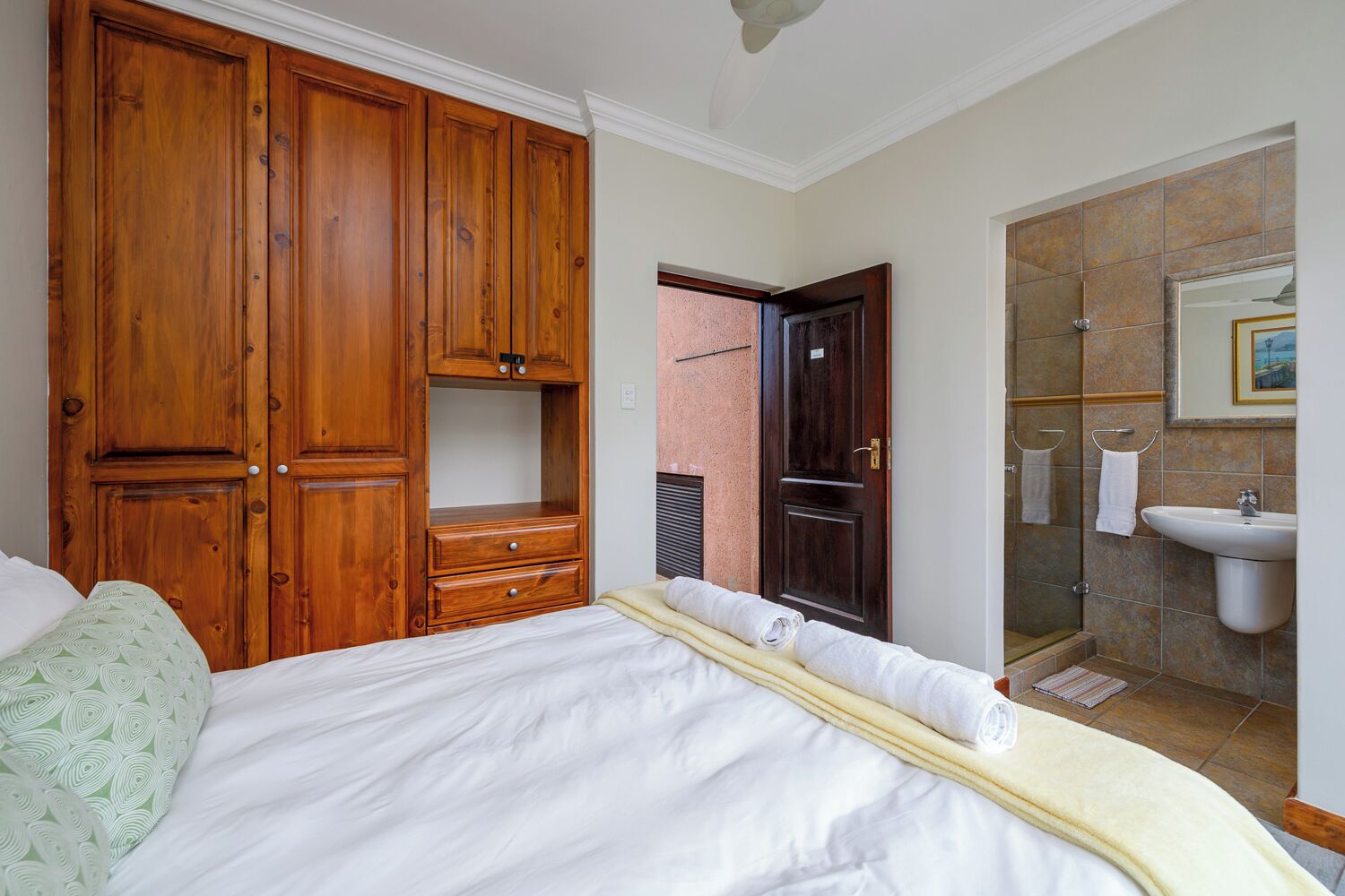 Een slaapkamer met een bed, een houten kledingkast en een badkamer met een wastafel en douche.