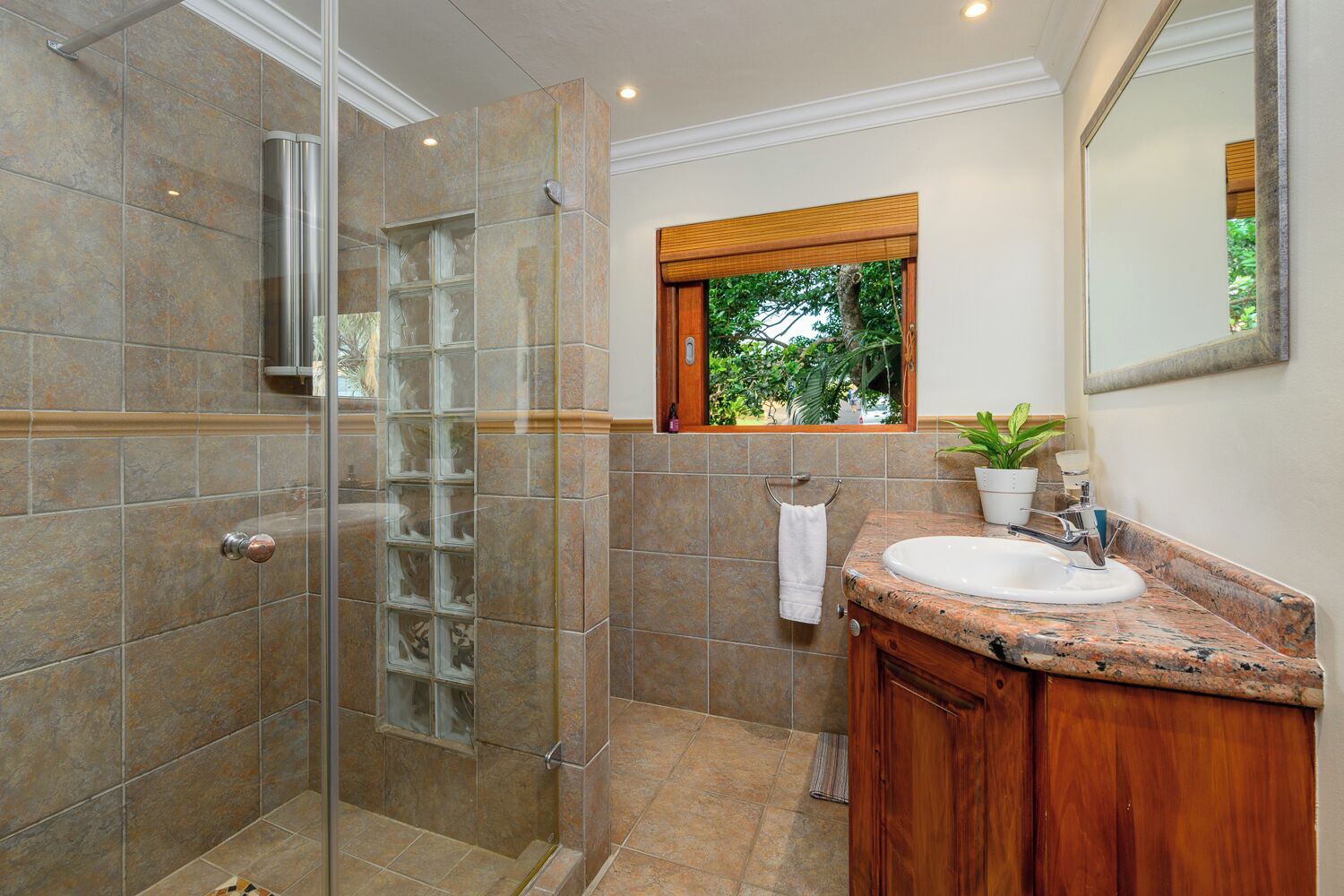 A bathroom with a glass shower enclosure, a sink with a wooden vanity, and a window with a view of greenery.