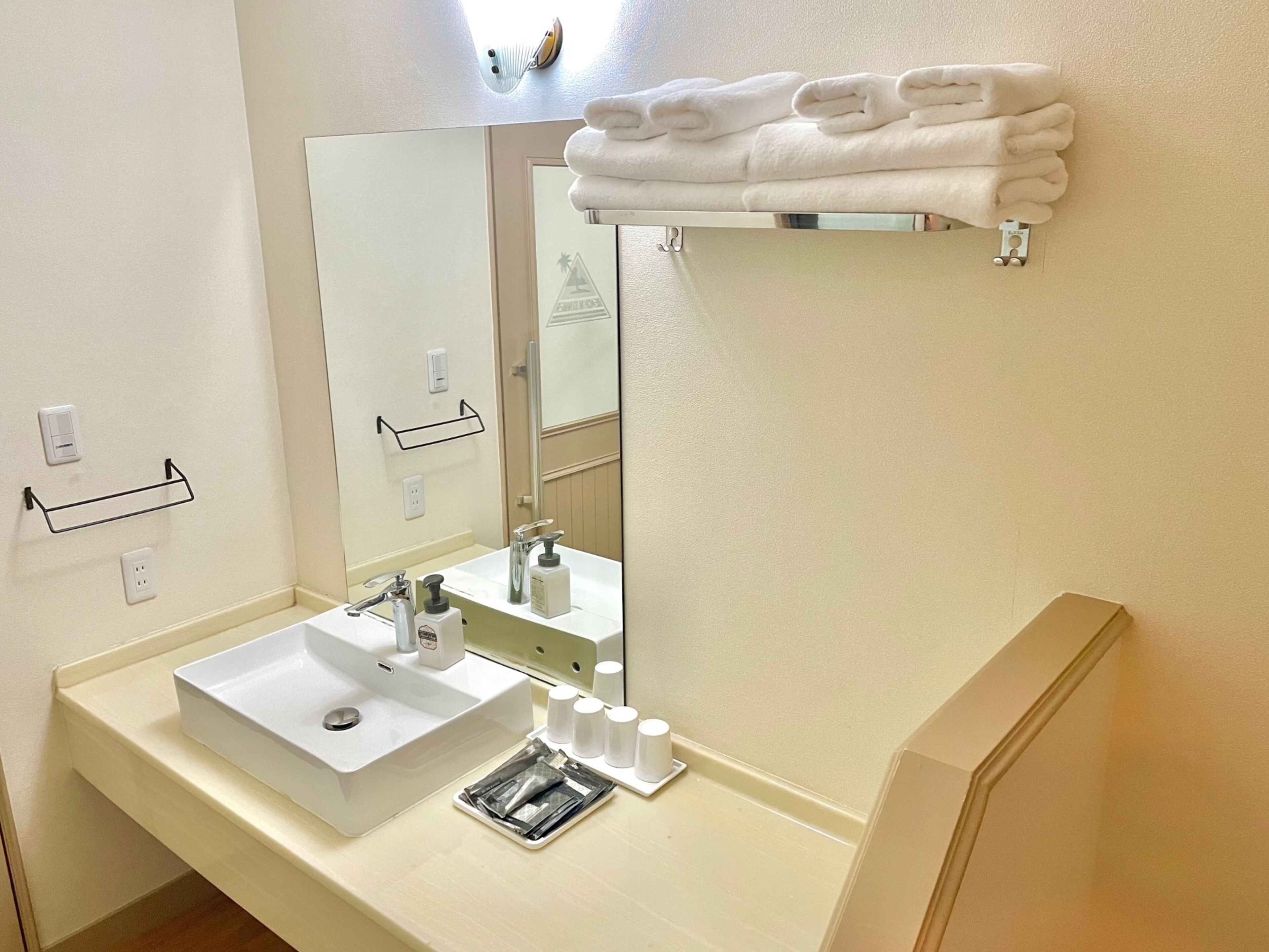 A bathroom with a white sink, mirror, towel rack, and a soap dispenser.