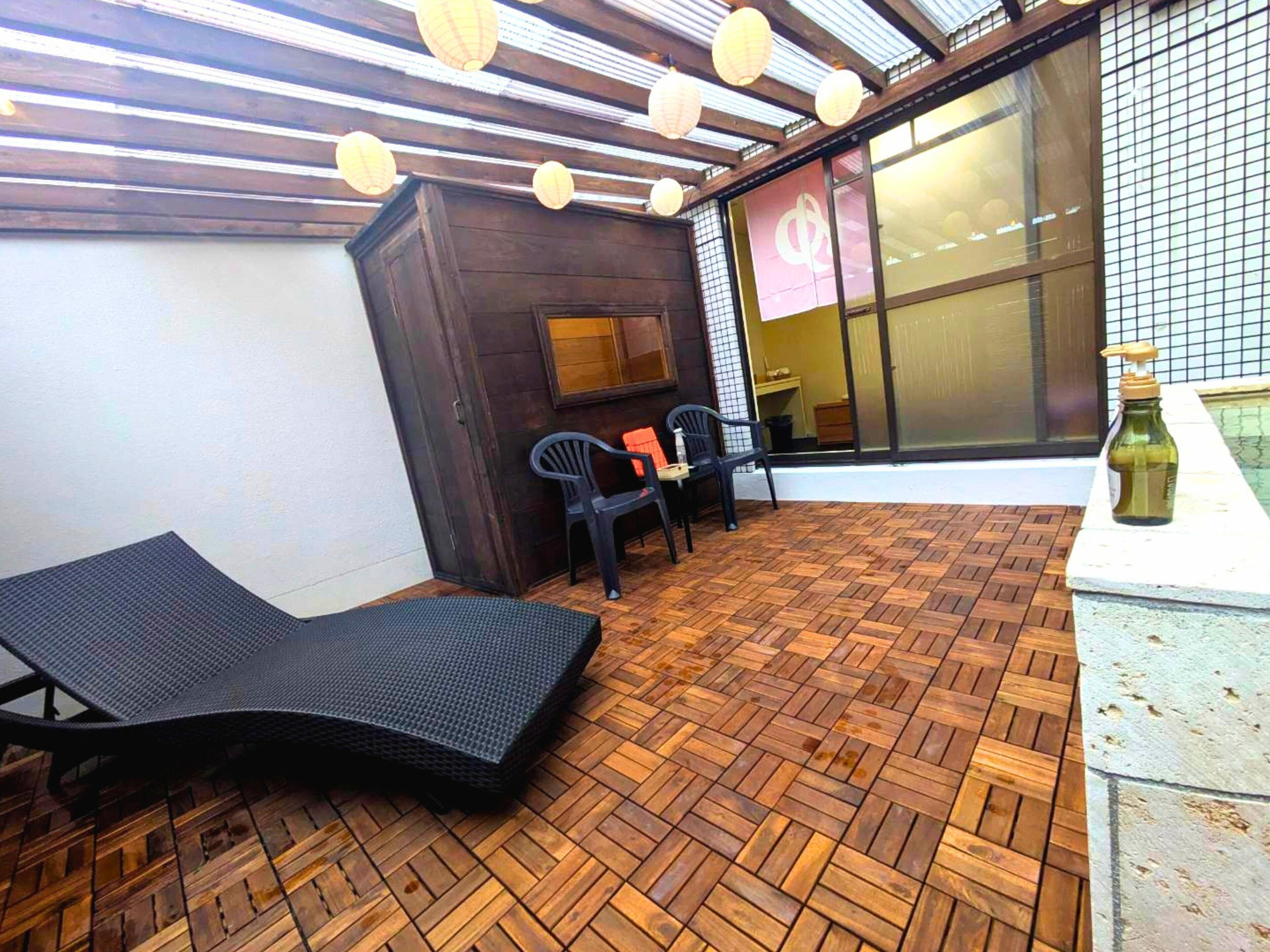 A sunlit patio with a herringbone floor, a lounge chair, two chairs, and a bottle of olive oil on a table.