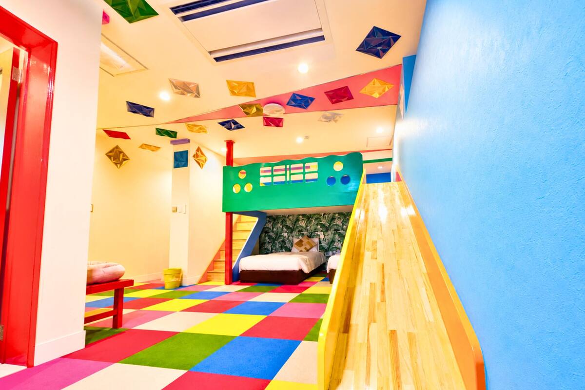 A colorful playroom with a bunk bed, a slide, and a checkered floor.