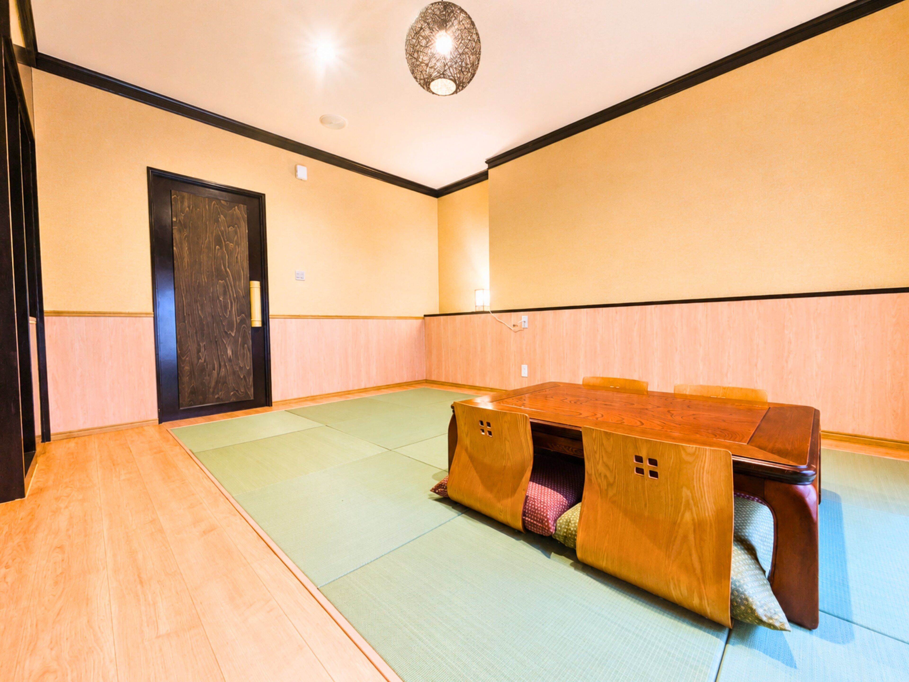 A conference room with a wooden table, tatami mats, a dark wooden door, and a ceiling light fixture.