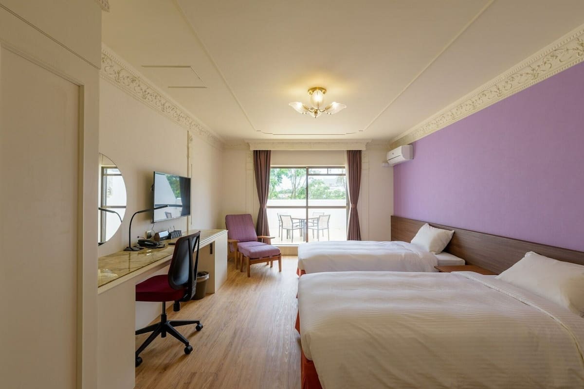 A hotel room with two beds, a desk with a computer, a chair, and a TV.