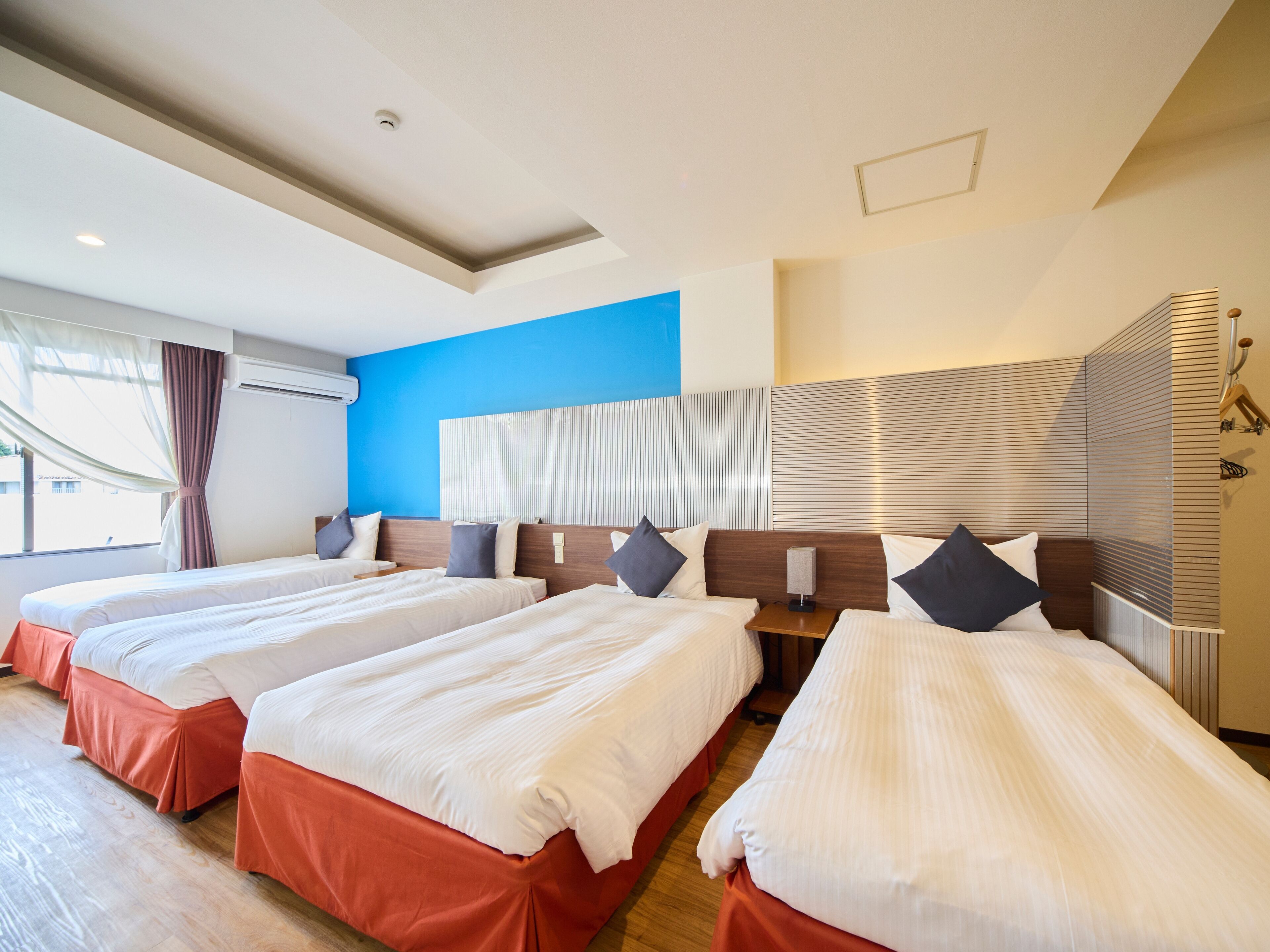 A hotel room with three beds, a blue accent wall, and a modern design.