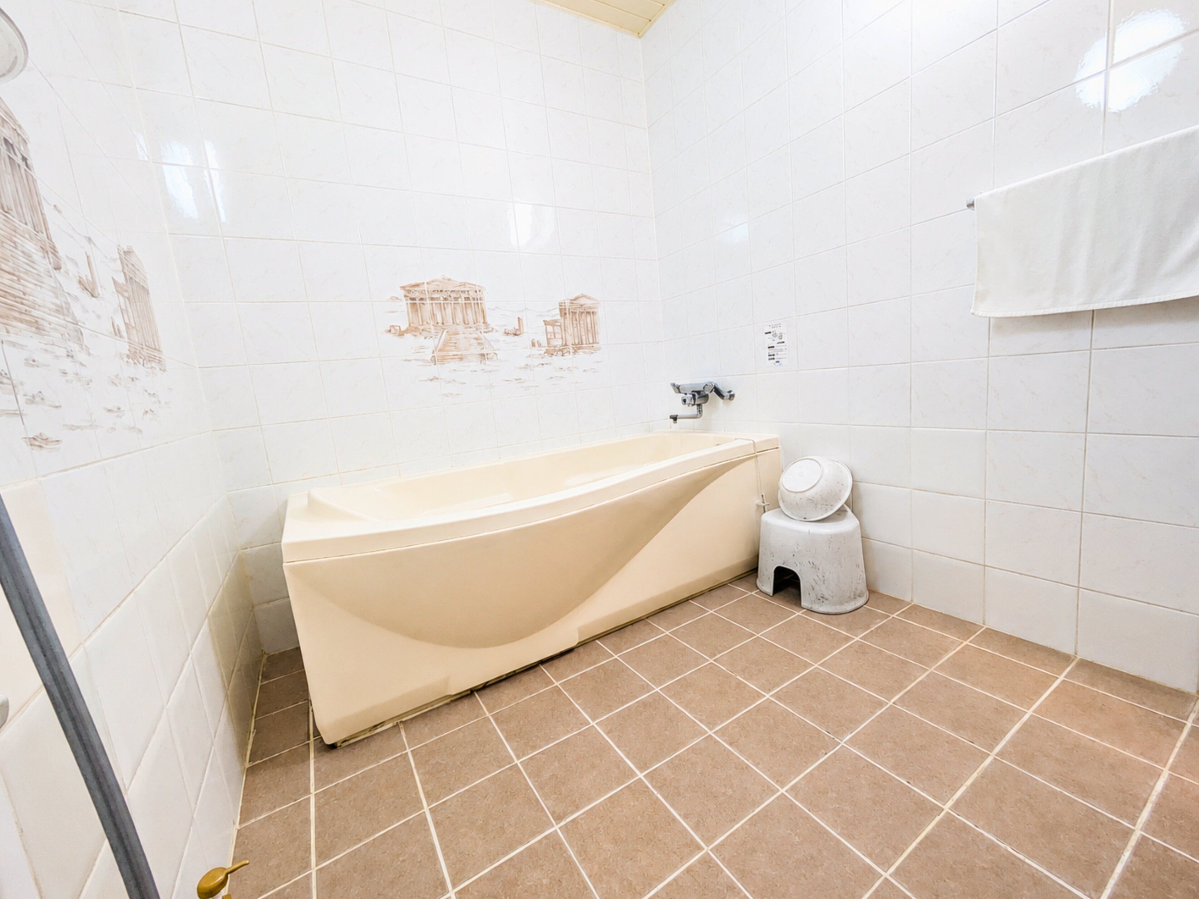 A bathroom with a bathtub, white tiles, and a small trash bin.