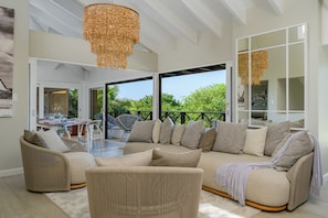 A spacious living area with a large sectional sofa, a wicker chair, and a hanging light fixture.