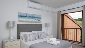 Quarto com cama, mesas de cabeceira, um quadro e vista através de uma grande janela.