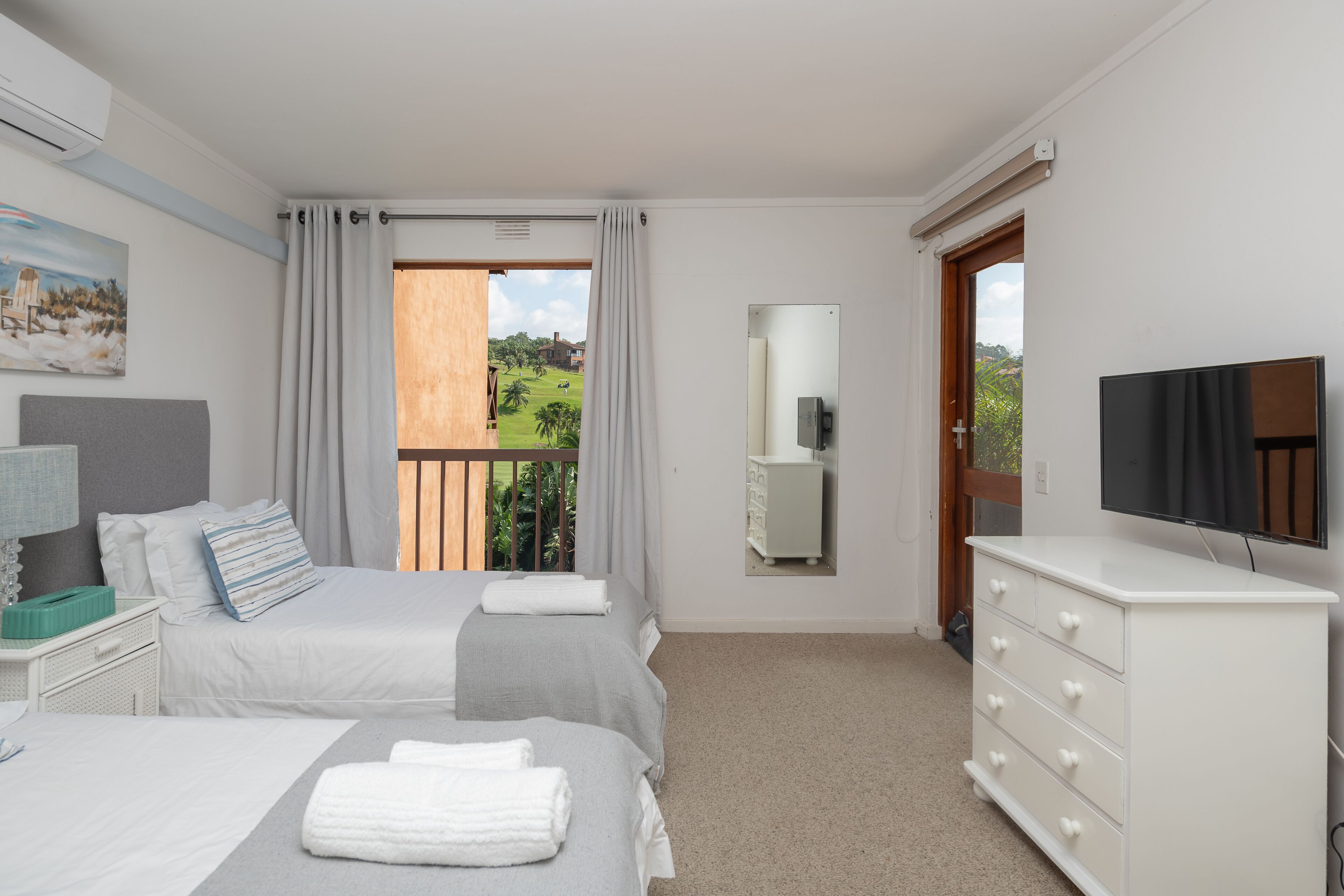 A bedroom with two beds, a dresser, a TV, and a window with curtains.