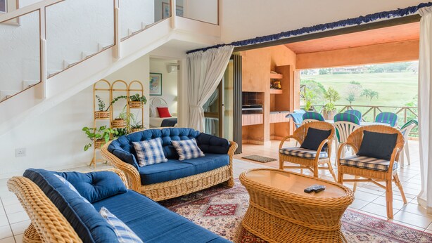 Uma sala de estar ampla com um sofá azul, cadeiras de vime e uma varanda com espaço para sentar ao ar livre.