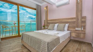 A bedroom with a large bed, a wooden headboard, a nightstand, and a view of the sea through a balcony. - Kas Otel (Kas)