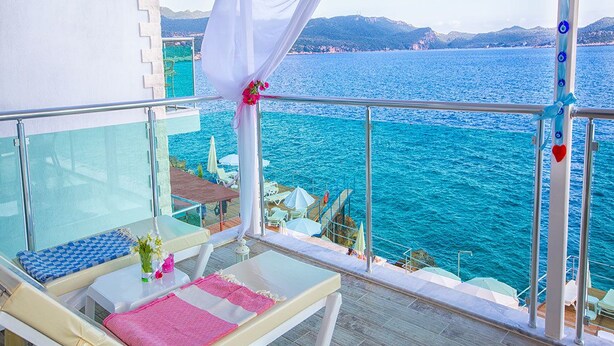 A balcony with a view of the sea, a table with a vase of flowers, and a chair with a pink towel. - Kas Otel (Kas)