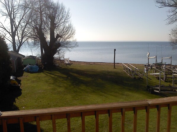 A grassy yard with a wooden deck, a tree, and a view of the water.