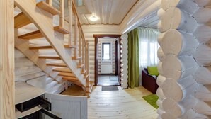 Eine Holztreppe führt zu einer Tür, eine Holzwand mit kreisförmigen Mustern und ein kleiner Küchenbereich mit einer Mikrowelle.