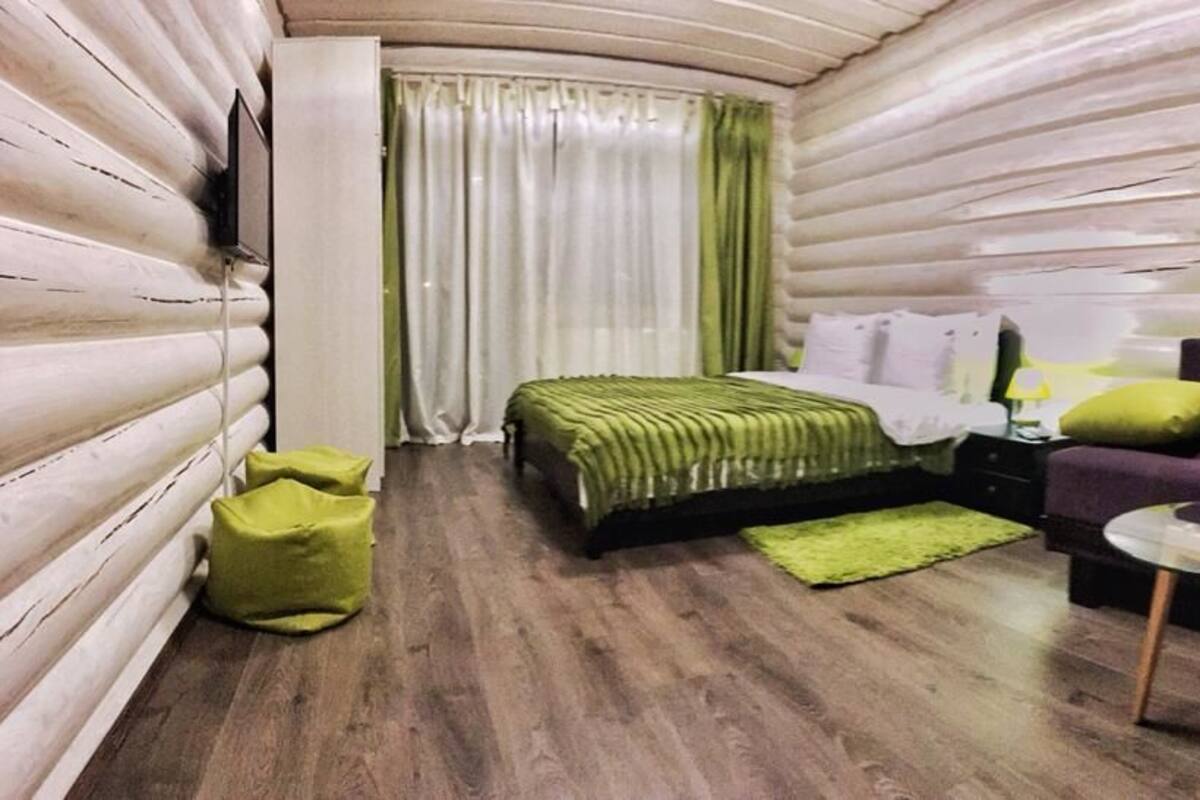 Habitación tipo cabaña de troncos con cama, sofá, una mesita y un tapete verde.