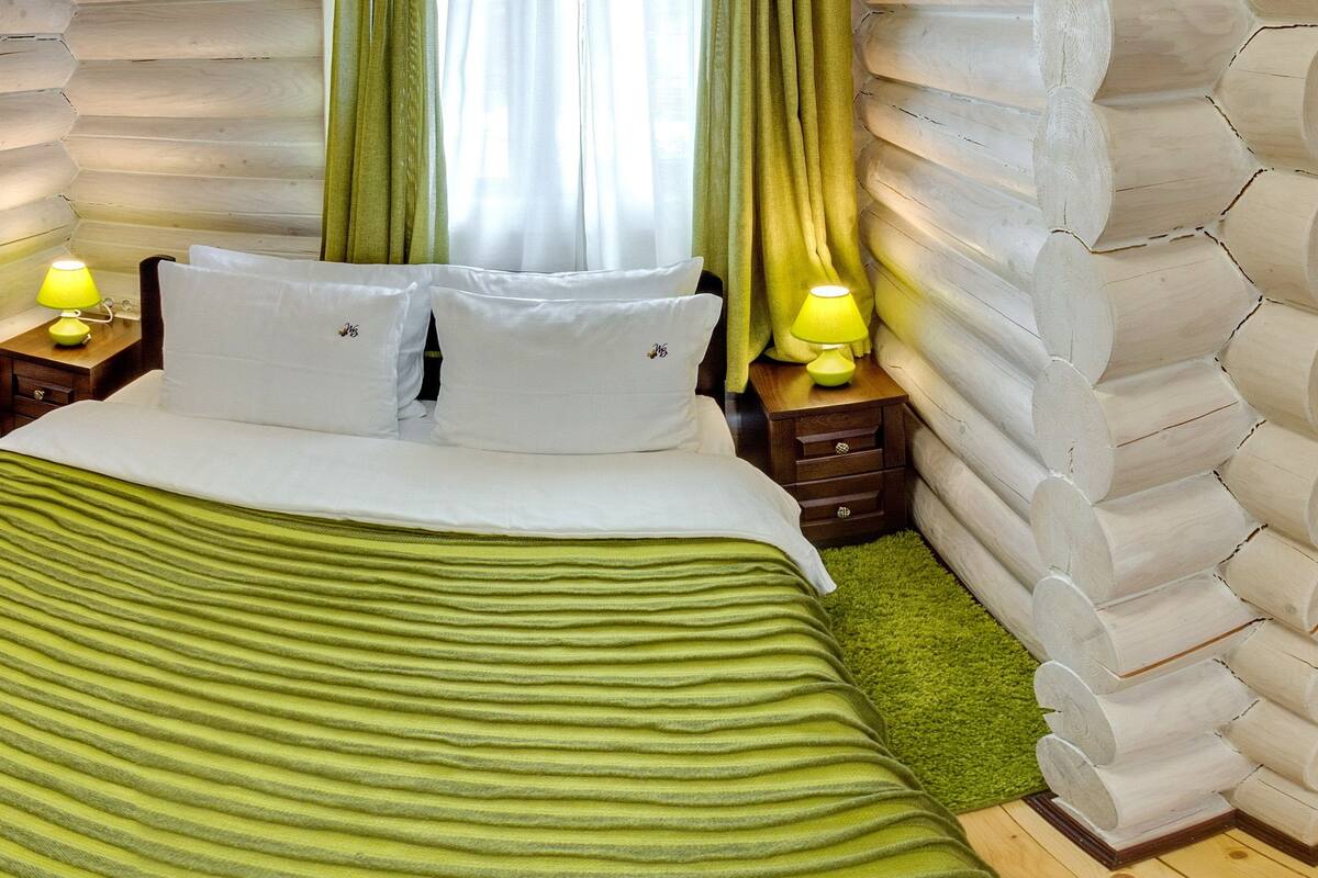 Una habitación con cama, ropa de cama verde a rayas, dos lámparas de noche y una cortina verde.