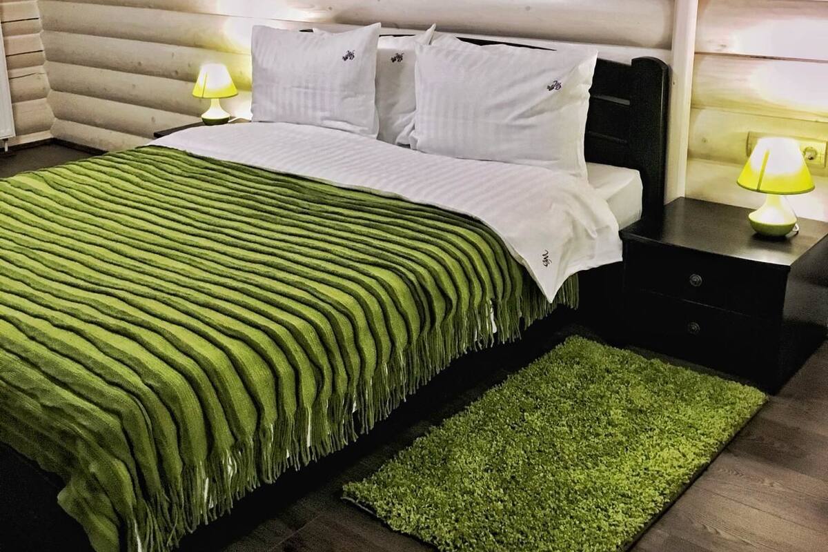 Una cama bien hecha con una colcha verde a rayas, dos lámparas de noche y una pequeña alfombra verde.
