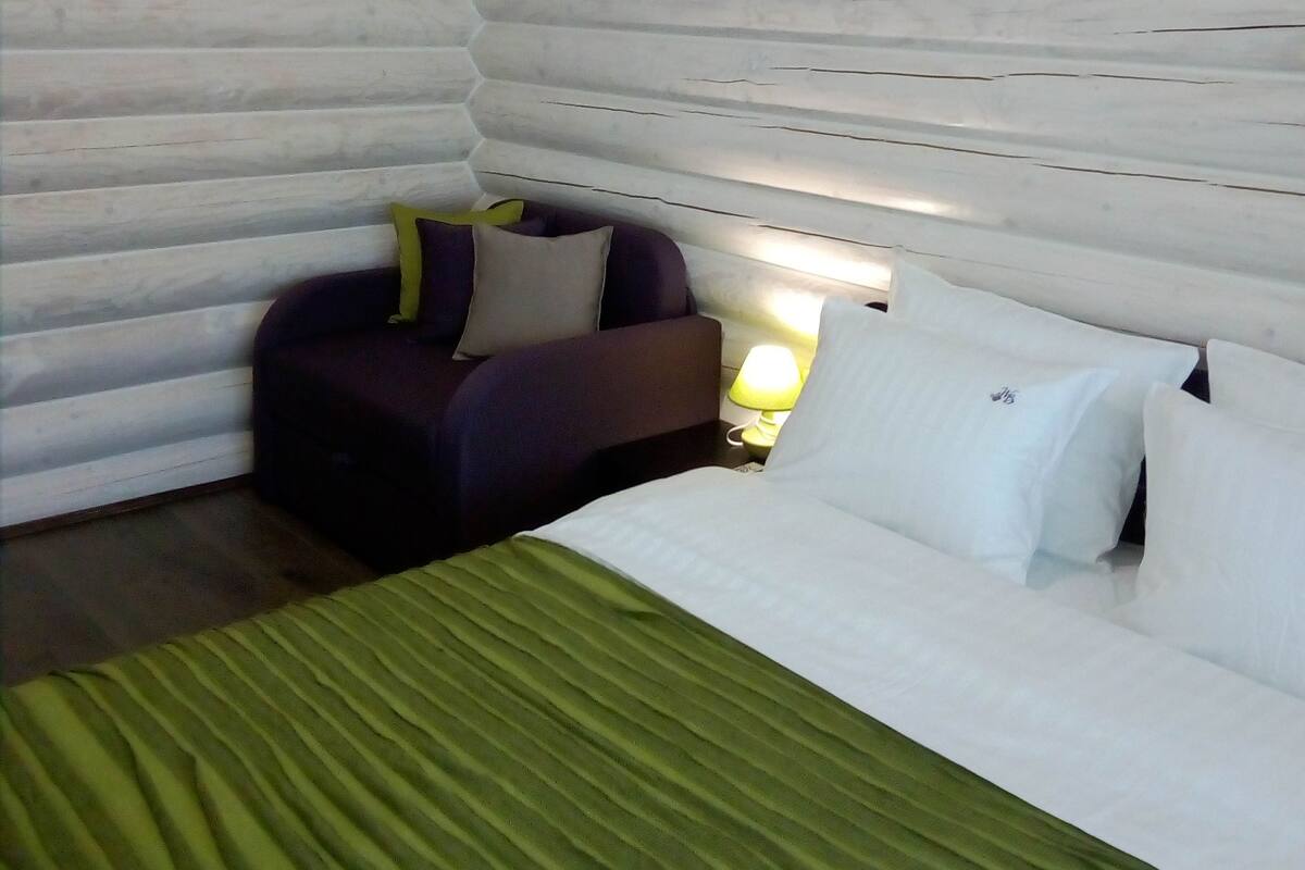 Una habitación tipo cabaña de troncos con una cama, un sofá y una mesita de noche con lámpara.