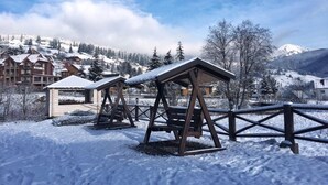 Schneebedecktes Freigelände mit Holzbauten, vermutlich Sitzgelegenheiten oder Schutzhütten, in einer Bergresort-Umgebung.