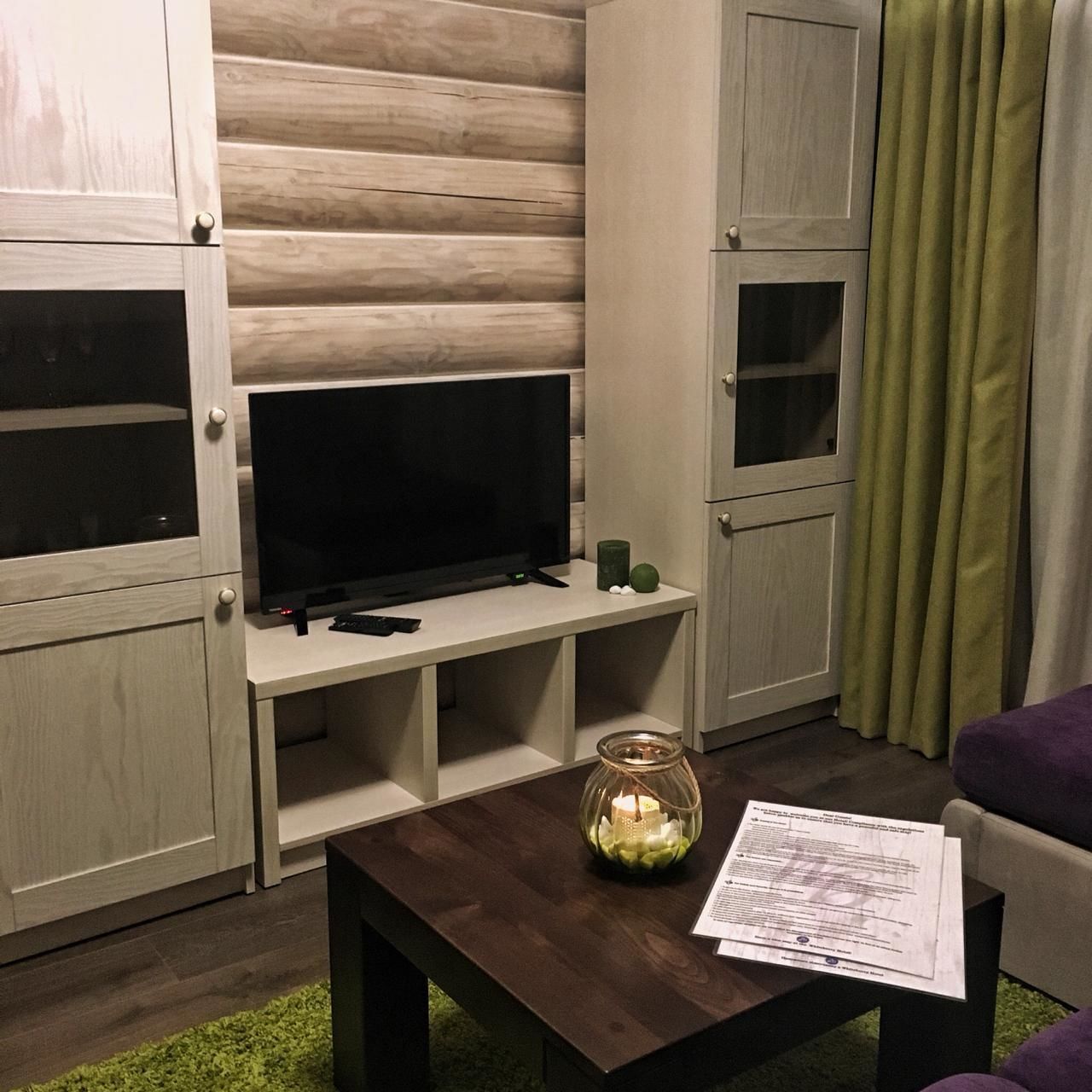 Un salon avec un téléviseur à écran plat posé sur un meuble en bois, une table basse en verre avec une bougie et un canapé.