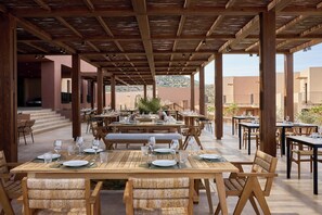An outdoor dining area with wooden tables and chairs, set against a backdrop of desert hills.