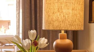 Une table de chevet en bois, une lampe, un vase avec des fleurs blanches et un vase plus petit.