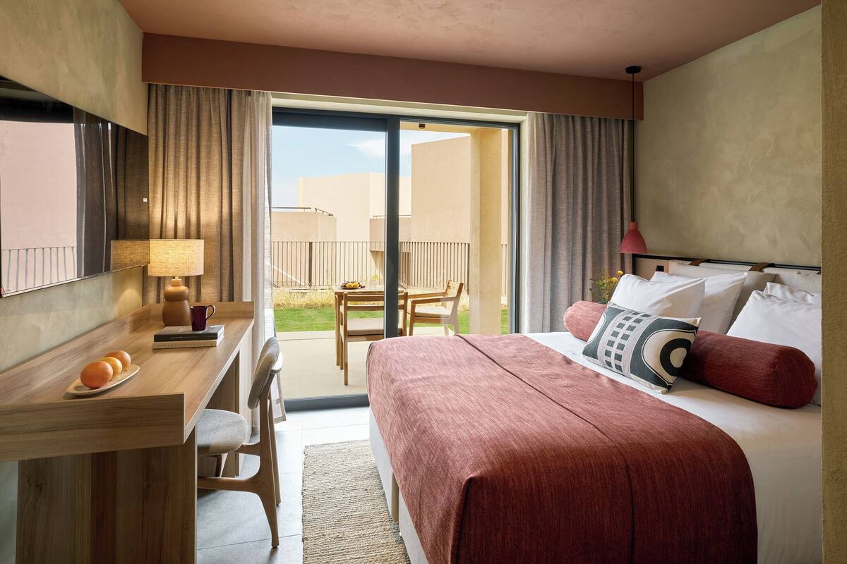 Ett hotellrum med en säng, ett skrivbord, en stol och en balkong med ett bord och stolar.