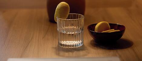 A wooden table with a lamp, a glass, and a bowl containing a lemon slice.