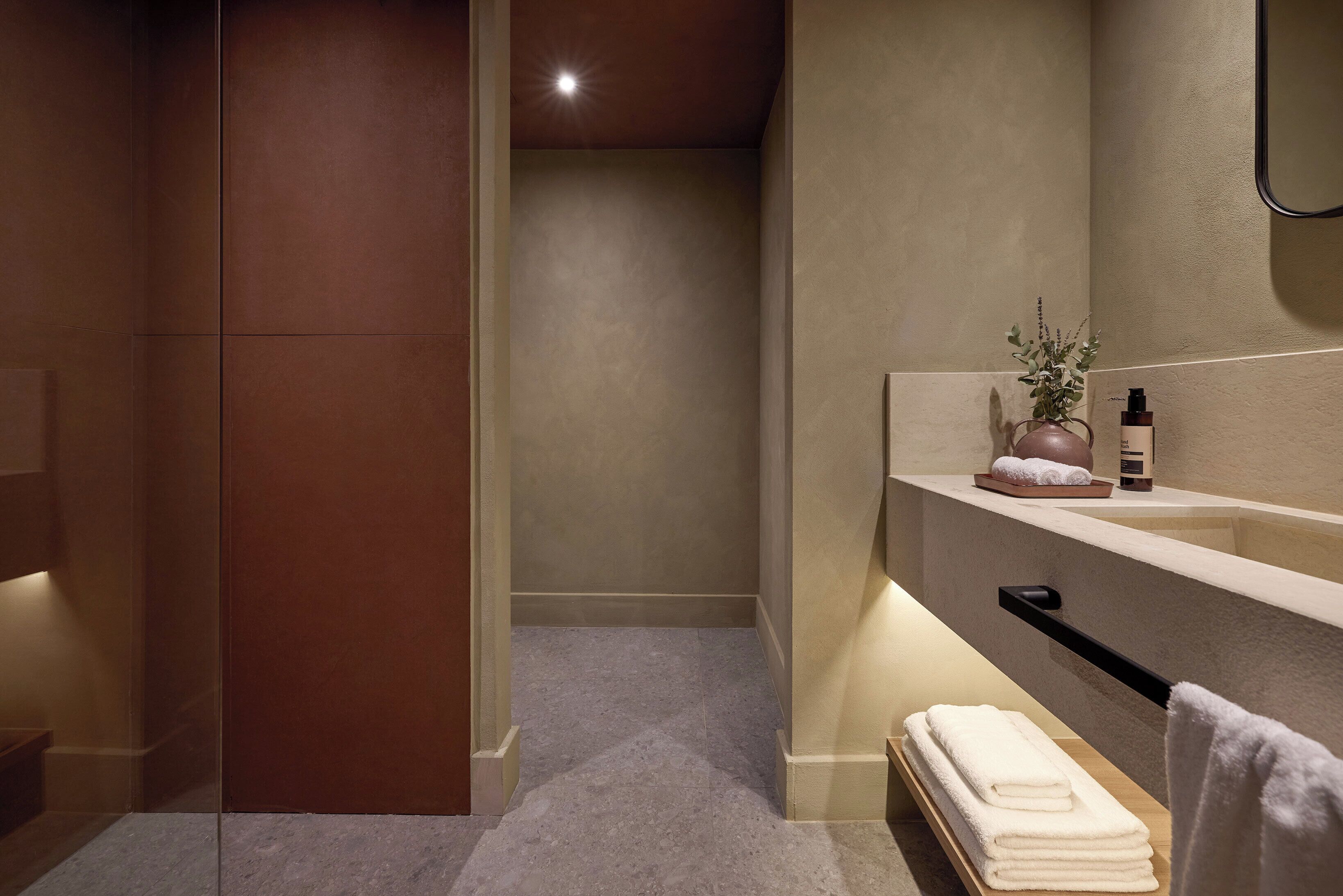 Une salle de bain moderne avec une douche à l’italienne en verre, un meuble-lavabo beige doté d’un porte-serviettes et une petite plante posée sur le plan de travail.