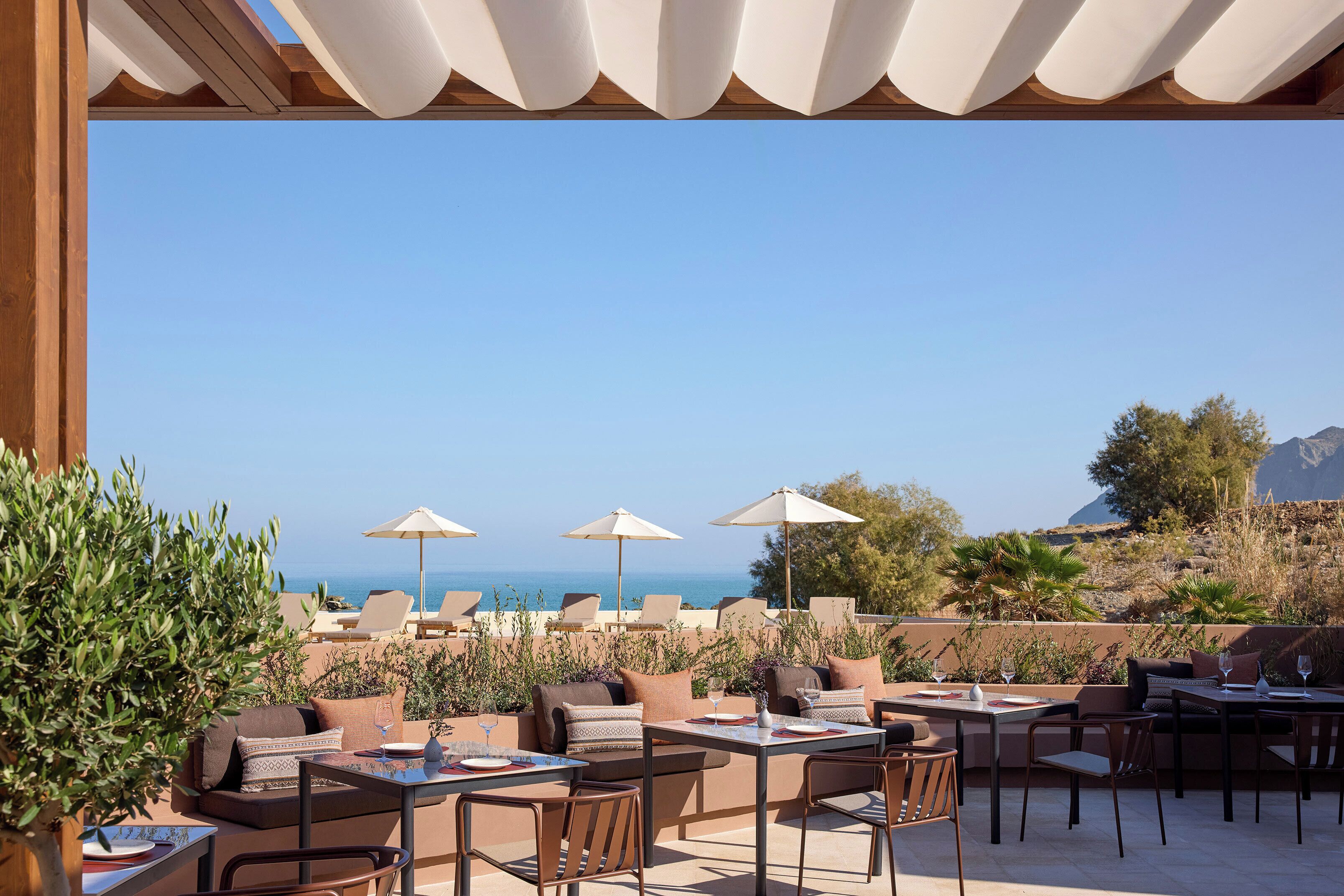 An outdoor seating area with tables and chairs, umbrellas, and a view of the sea.