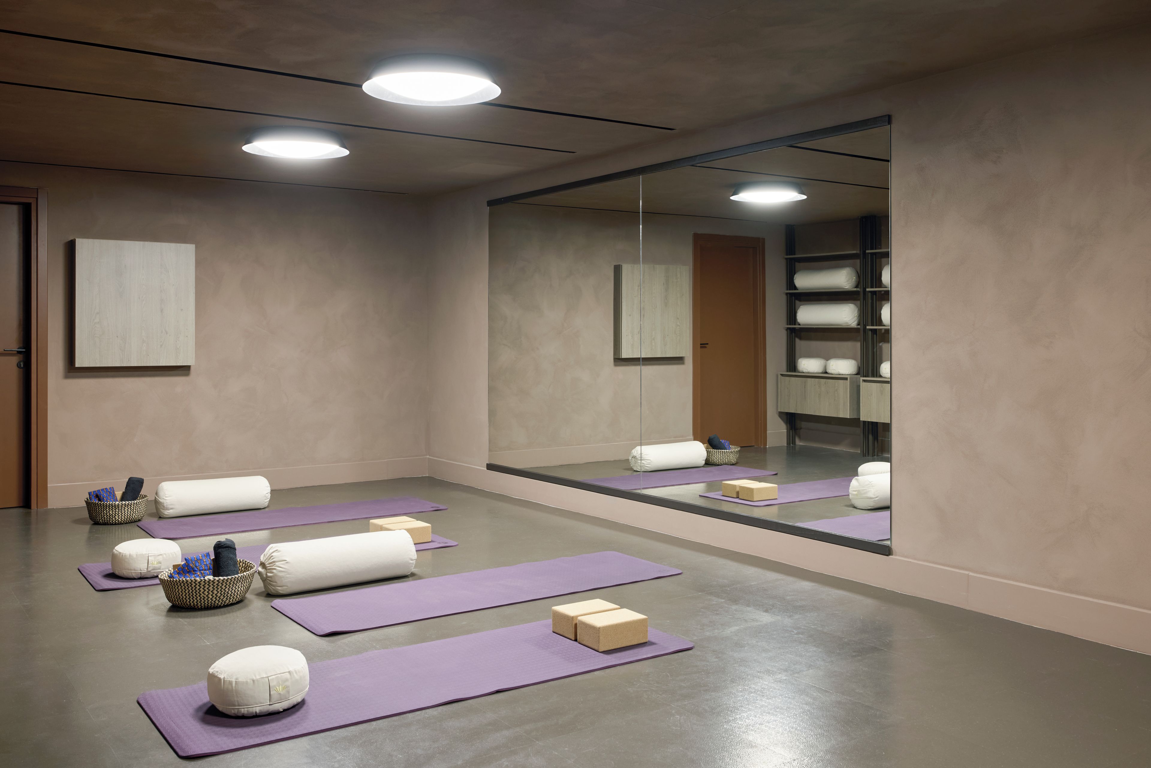 Quarto com espelho grande, tapetes de yoga e prateleira com toalhas.