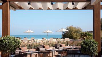 Un espace extérieur aménagé avec des tables et des chaises, offrant une vue sur une plage et la mer.