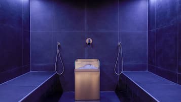 A modern bathroom with dark blue tiles, a central sink with a soap dispenser, and two showerheads.