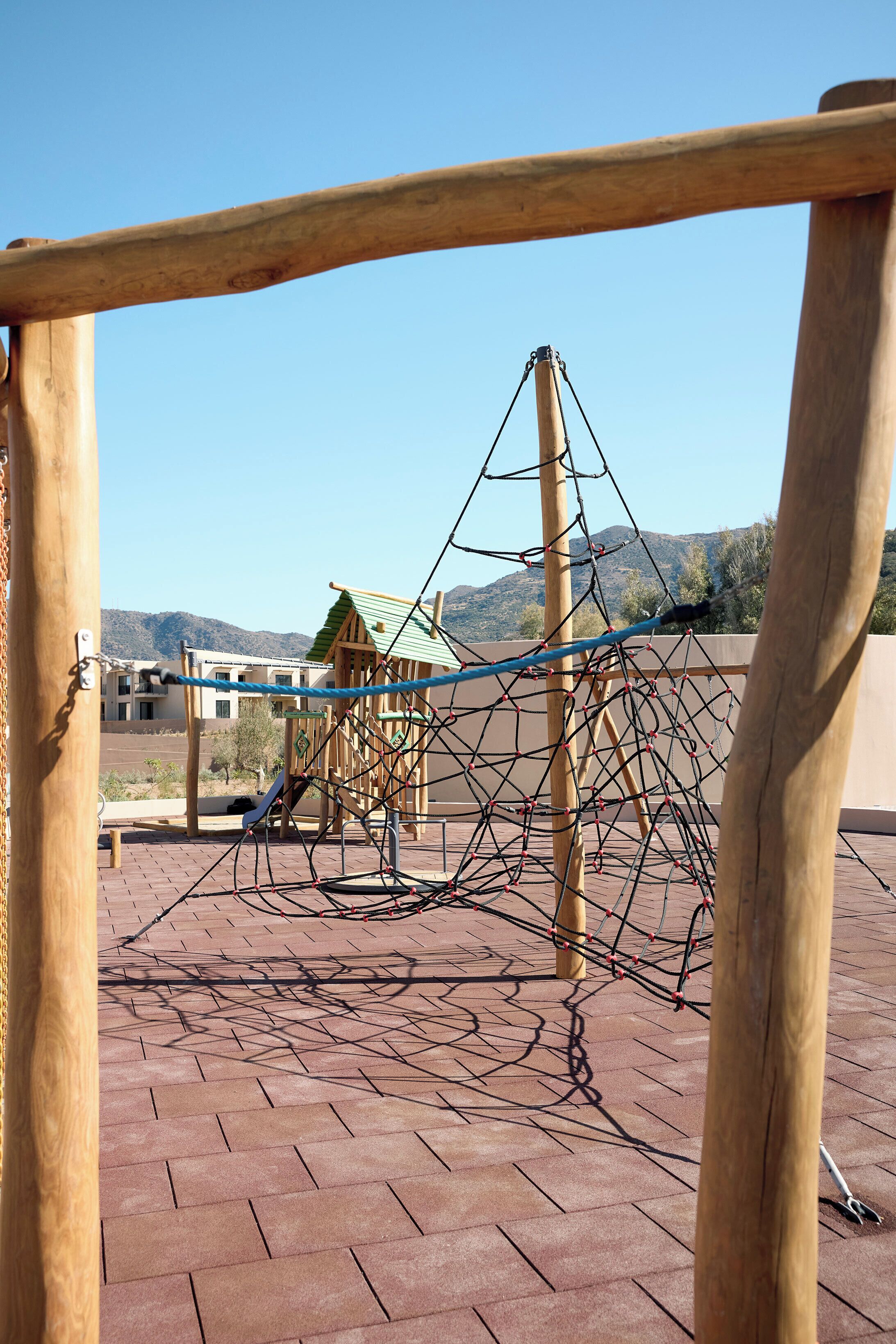 A wooden play structure with a rope net, set on a brick patio with a mountain view in the background.