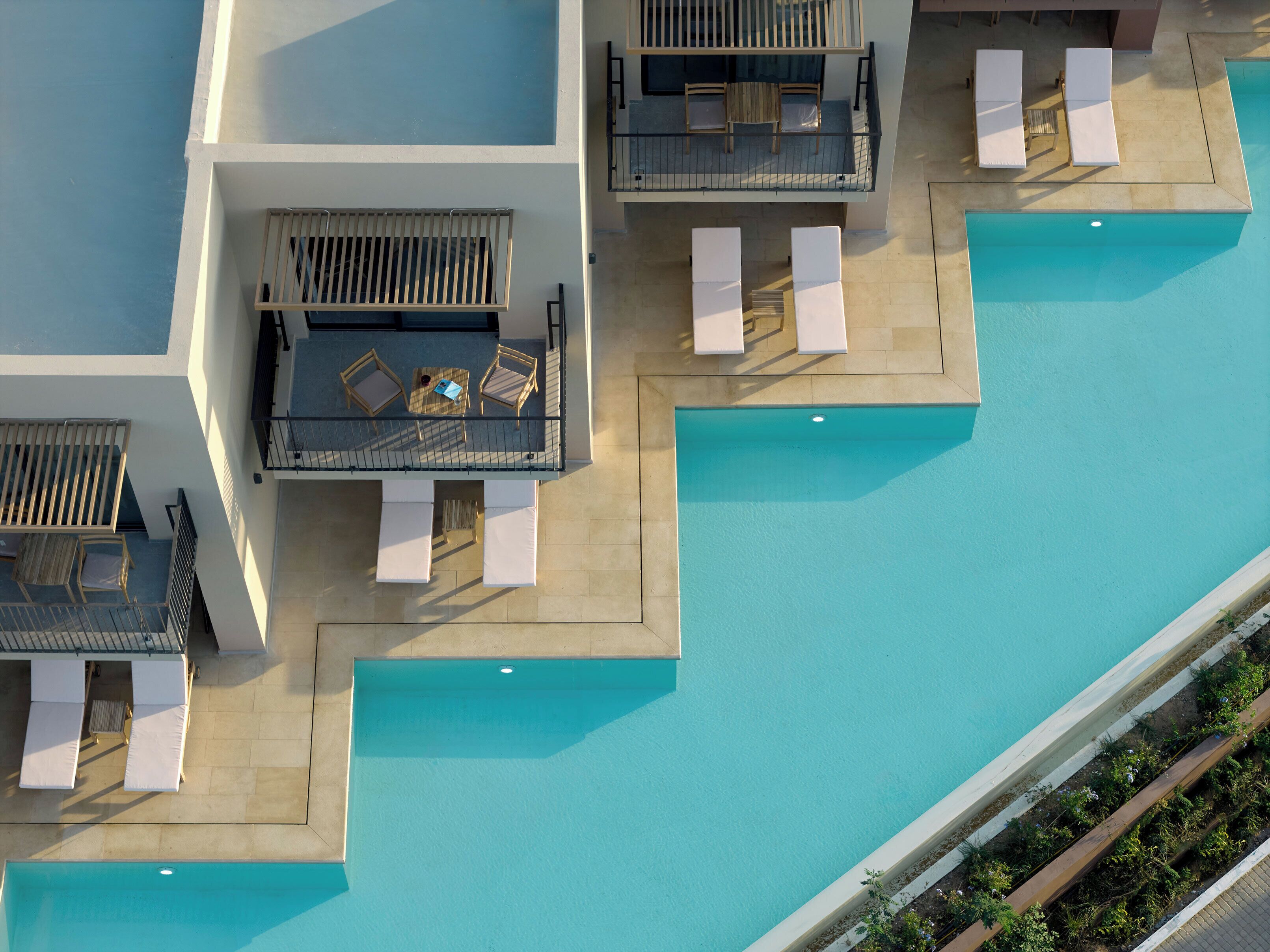 An aerial view of a hotel with multiple swimming pools, sun loungers, and a covered seating area with tables and chairs.