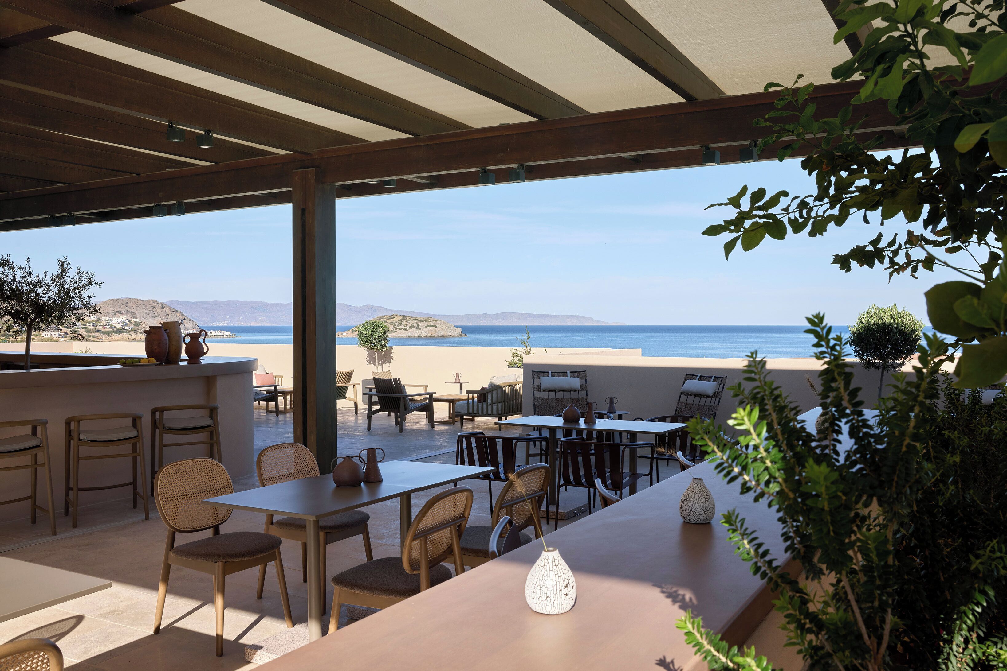 An outdoor patio with tables and chairs, overlooking a beach and the sea.