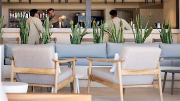 Zona de bar con sofás y sillones, una barra con botellas y plantas verdes.