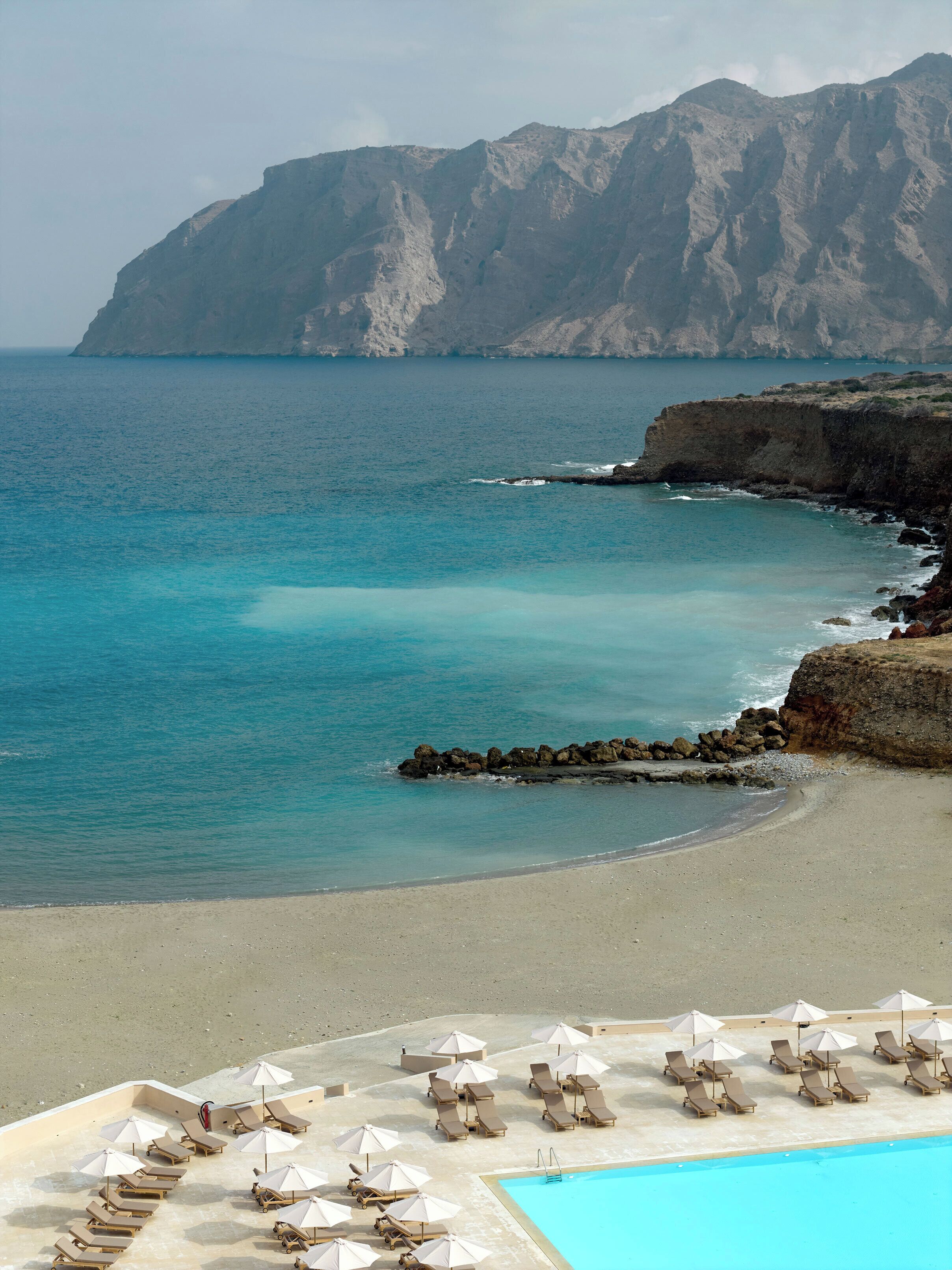 A beach resort with a pool area, sun loungers, and umbrellas.