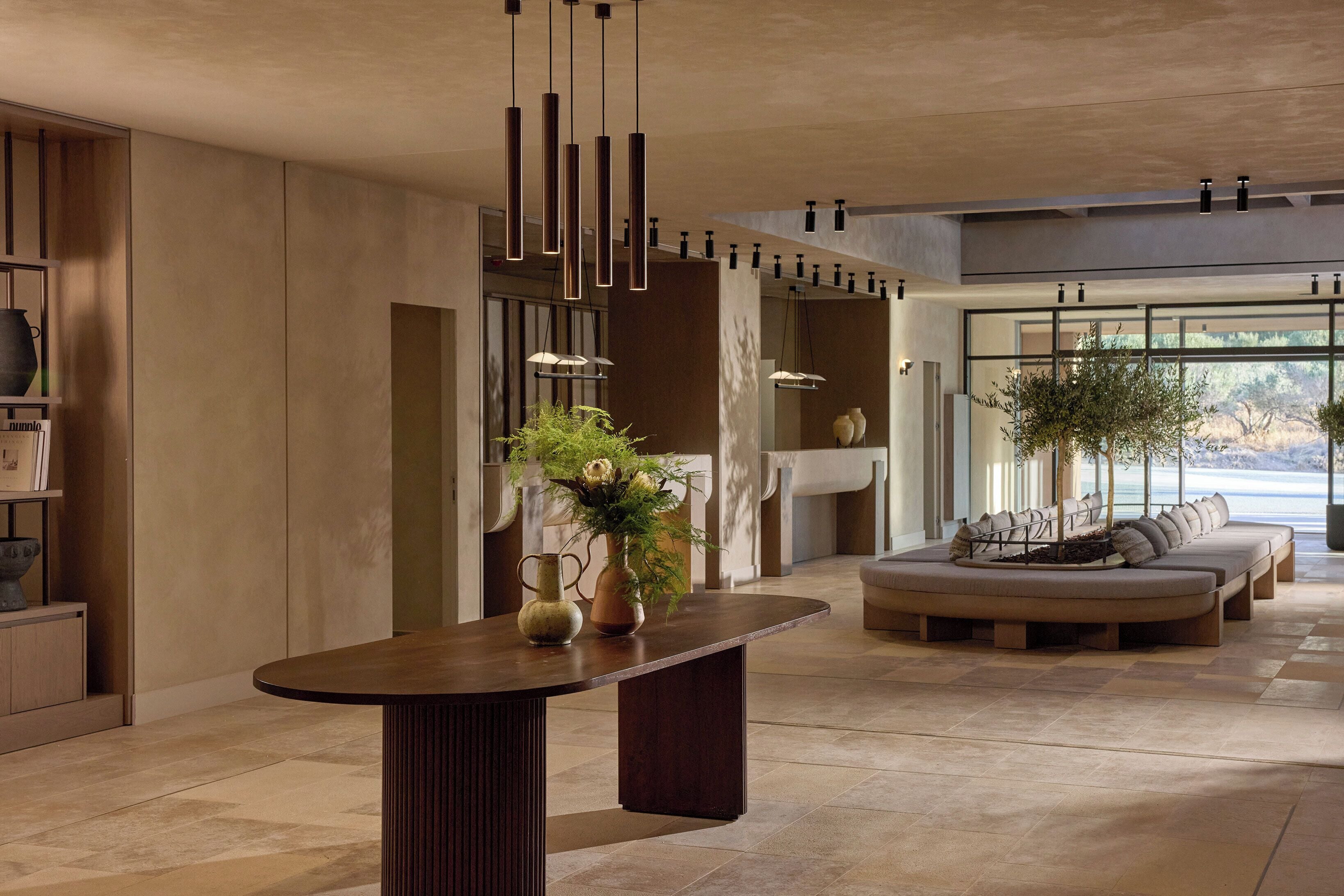 A modern interior with a central table, seating area, and hanging lights.